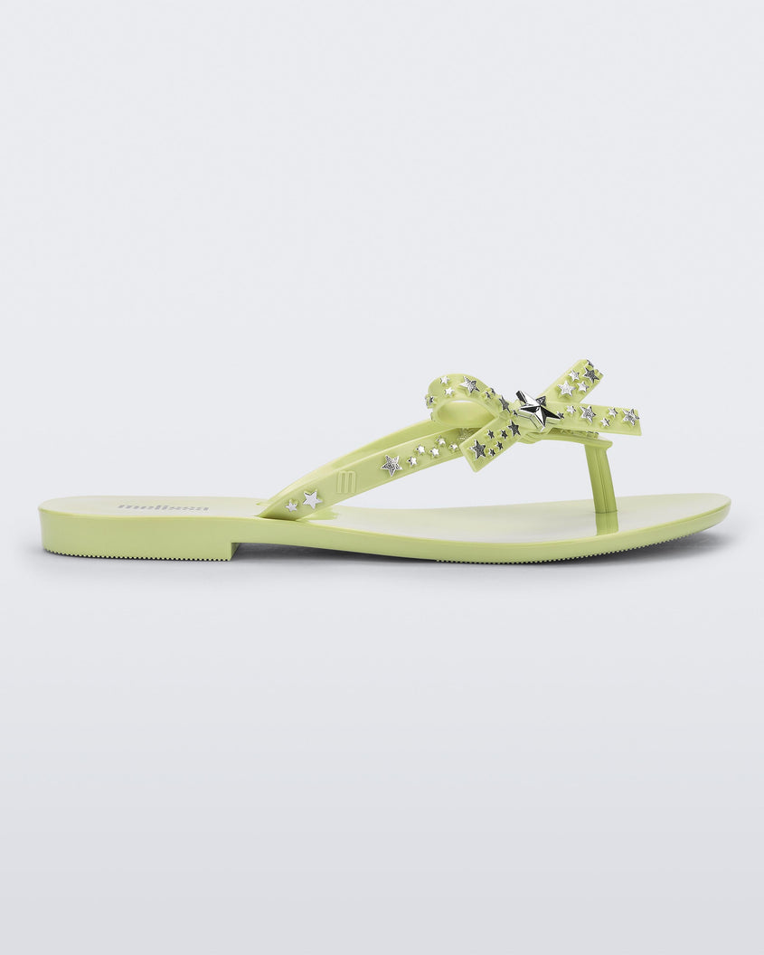 Side view of a green Harmonic Stars flip flops with a bow and silver star details on the straps.