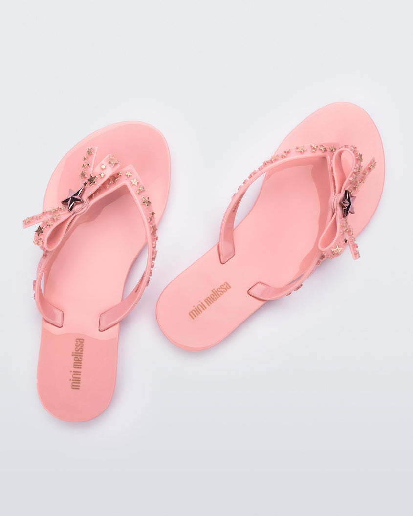 Top back view of a pair of pink Mini Melissa flip flops with a bow and gold star details on the straps.