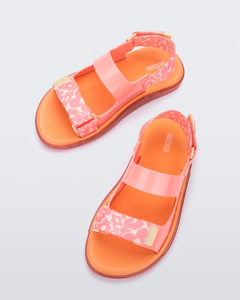 A top view of a pair of pink Melissa Brave Papete sandals with an orange insole, pink flower print, pink straps and a velcro back.