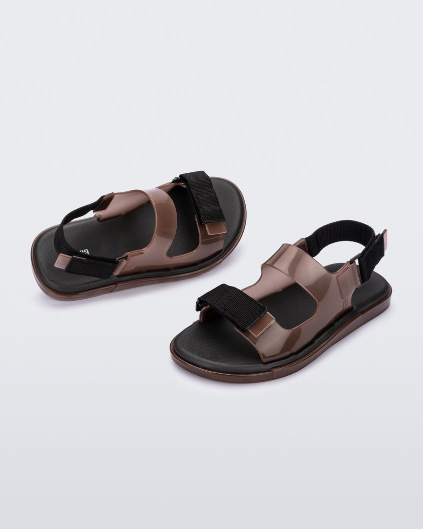An angled front and side view of a pair of brown Melissa Brave Papete sandals with two straps, a brown base, black sole, and a front and back black velcro strap.