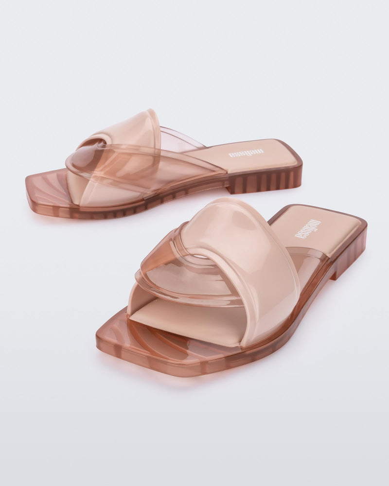 An angled front and side view of a pair of pink Melissa Brigitte slides with a solid and transparent weft designed upper strap.