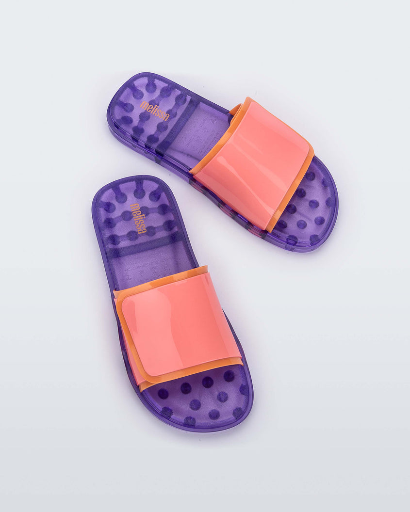 Top view of a pair of lilac/pink Melissa Brave Slides with a pink and orange velcro top strap and translucent lilac insole.