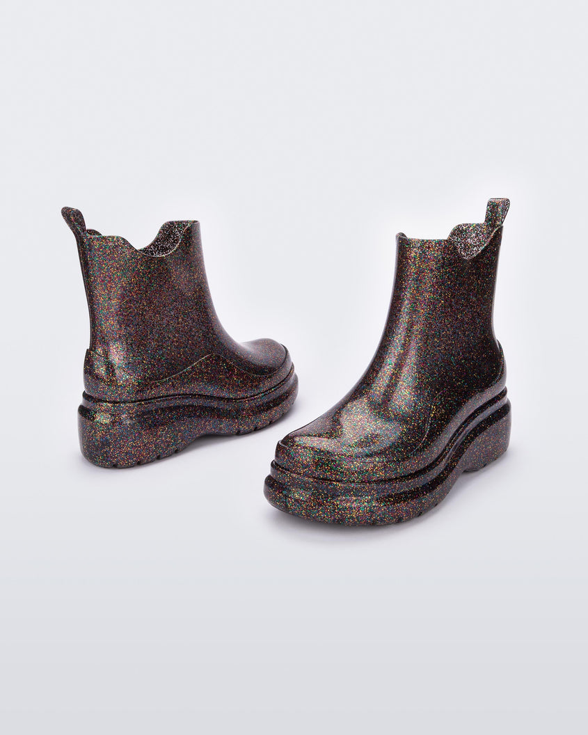 An angled side and front view of a pair of clear glitter black Melissa Grip multicolor glitter short rain boots.
