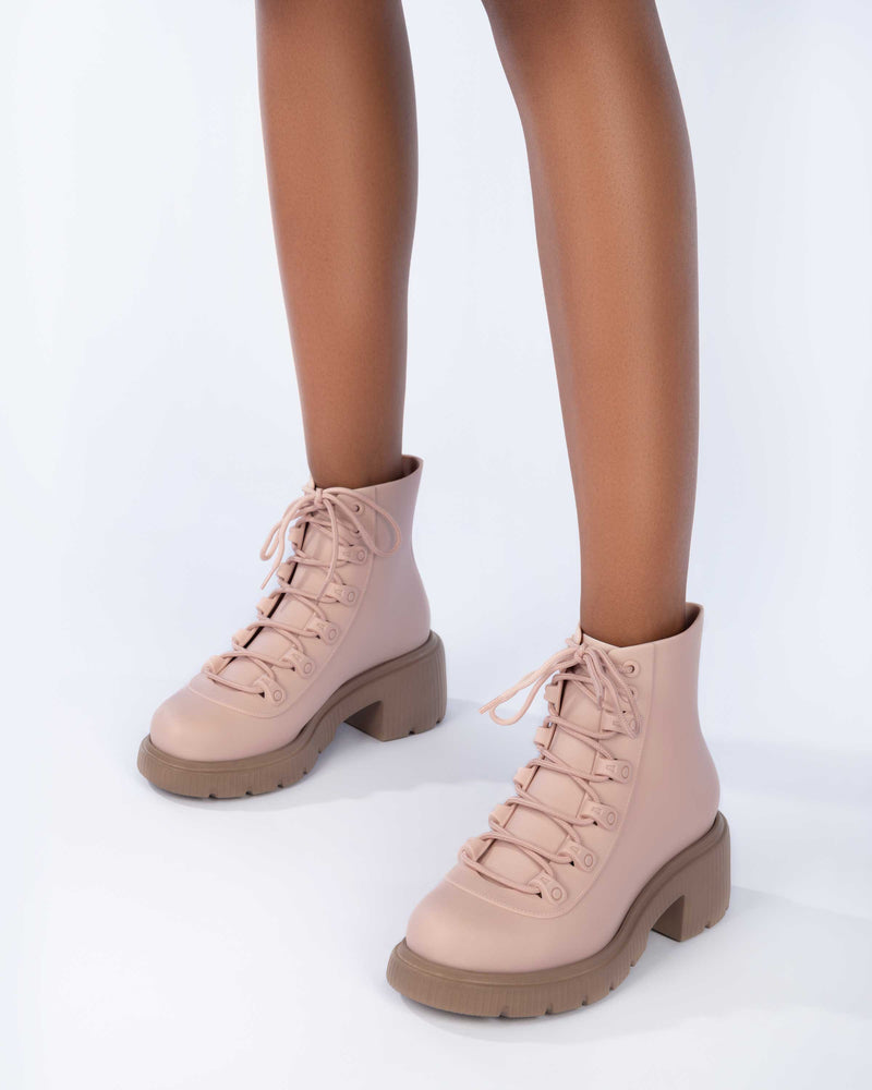 A model's legs wearing a pair of brown/pink Melissa Cosmo boots with a pink base, laces and a brown heel sole, laying on their side.