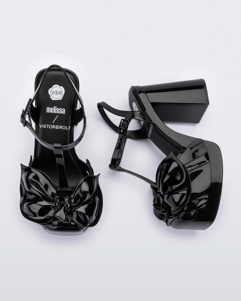 A top and side view of a pair of black Melissa Tie Party Heels with several straps and a bow on the toe.