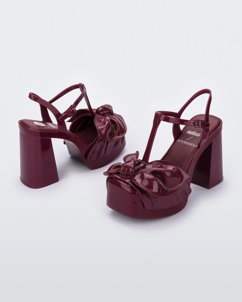 An angled side and back view of a pair of red Melissa Tie Party Heels with several straps and a bow on the toe.