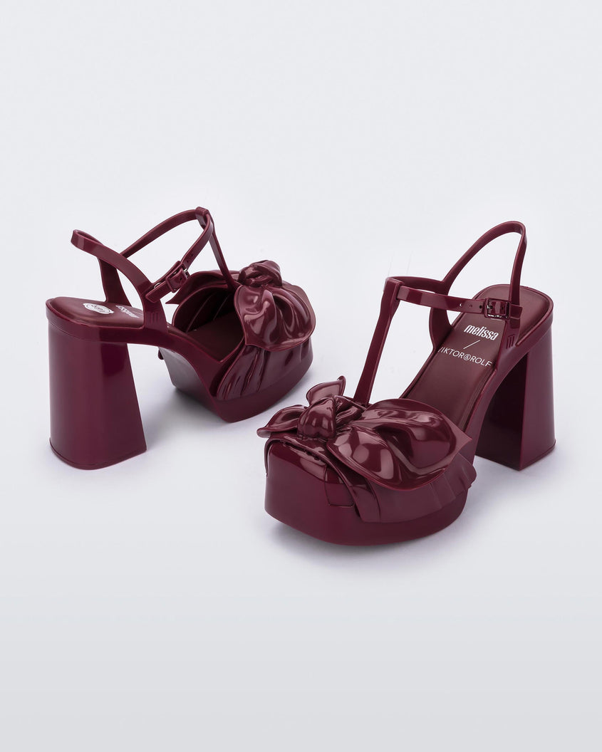 An angled side and back view of a pair of red Melissa Tie Party Heels with several straps and a bow on the toe.