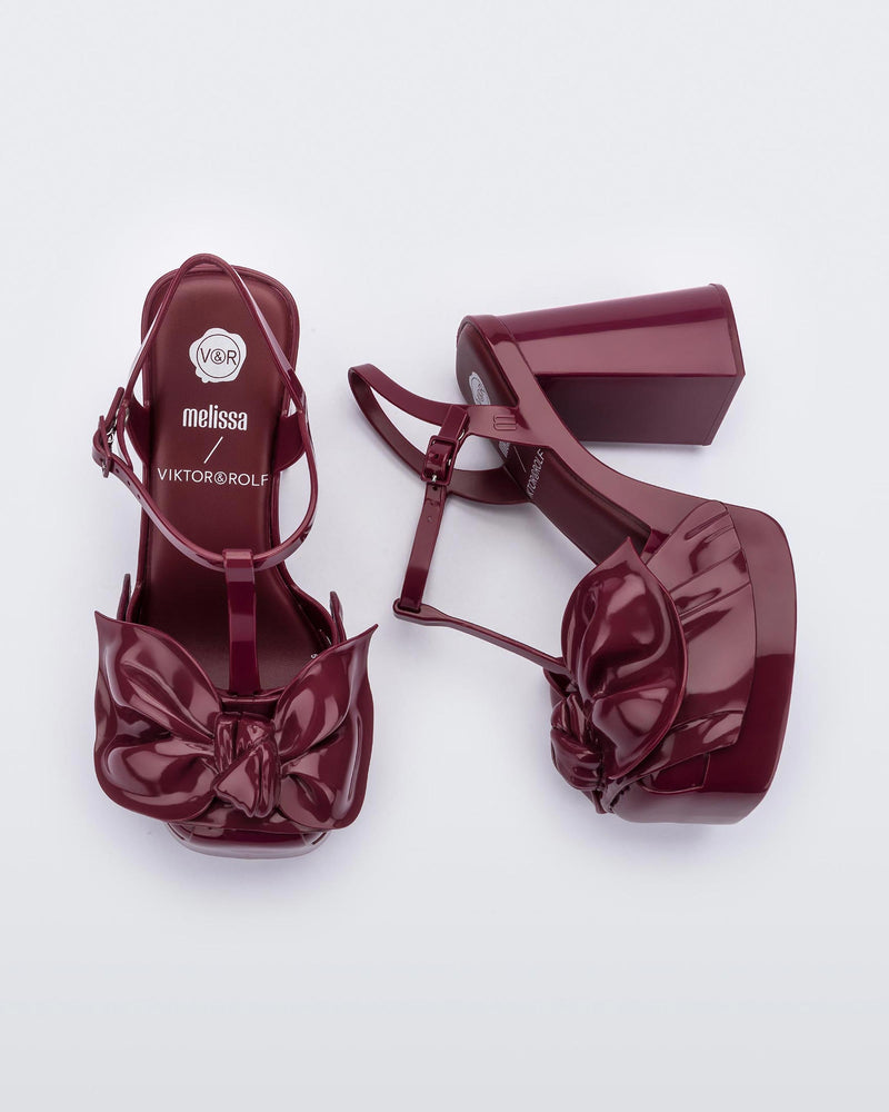 An top and side view of a pair of red Melissa Tie Party Heels with several straps and a bow on the toe.