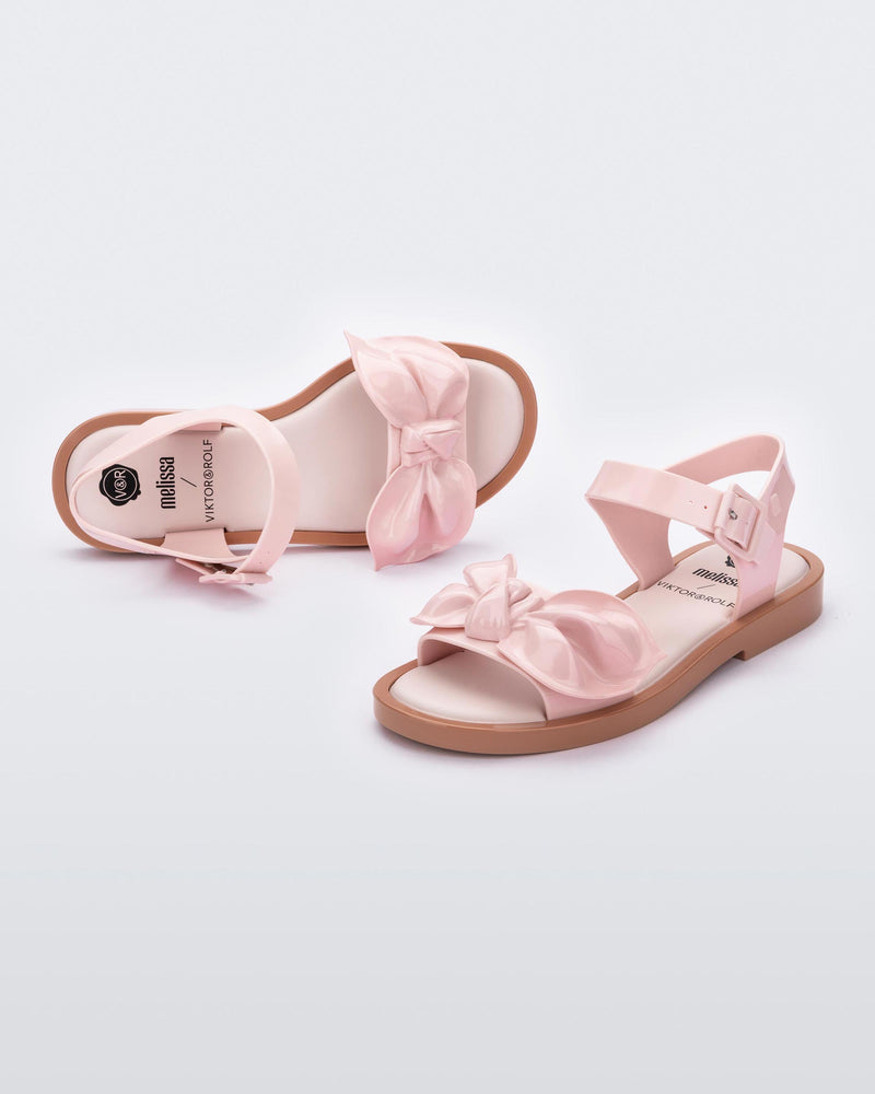 Front and back view of a pair of Melissa Tie Mar sandals with beige sole, pink ankle straps with buckle closure and pink 3D bow detail on front straps