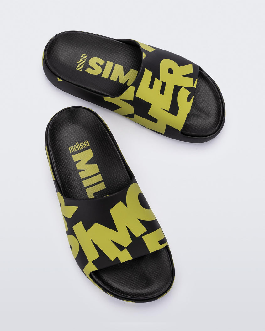 A top view of a pair of Black & Kiwi Logo Scramble Melissa Cloud slides with a green simon miller letter scrambled text on the base and a black insole reading in green