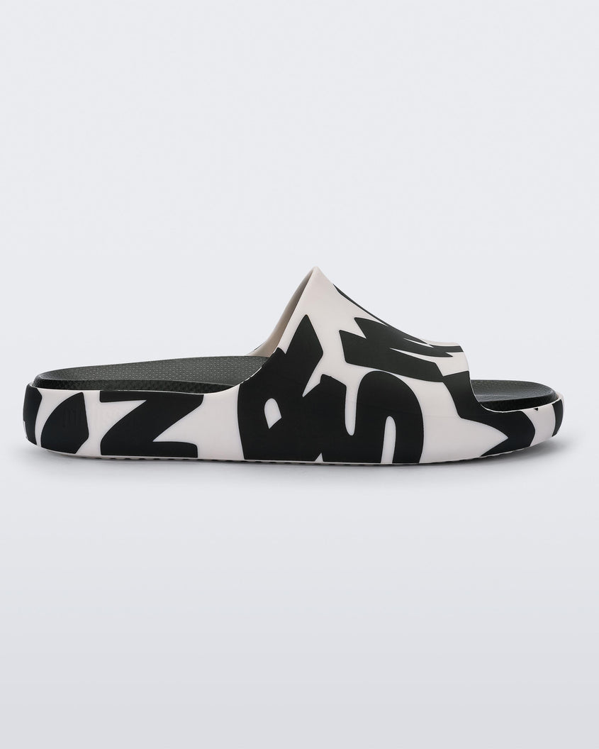Side view of a White Logo Scramble Melissa Cloud slides with a black simon miller letter scrambled text on a white base base and a black insole reading in red