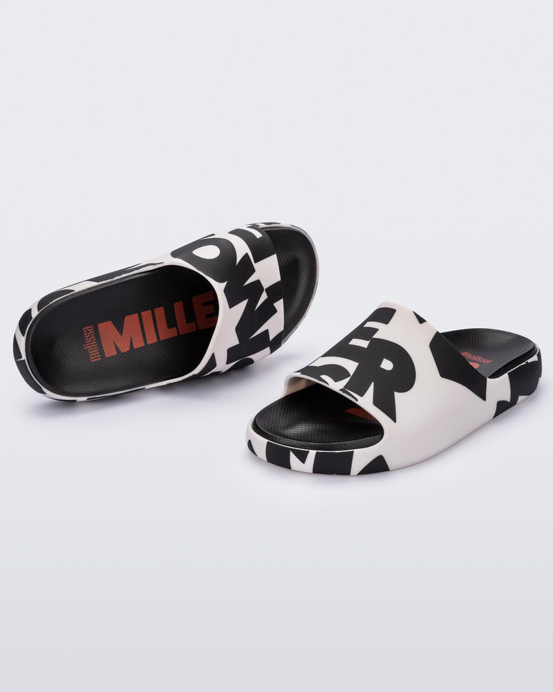 An angled top and front view of a pair of White Logo Scramble Melissa Cloud slides with a black simon miller letter scrambled text on a white base base and a black insole reading in red "Melissa Miller" and "Melissa Simon" on different shoes