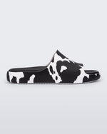Side view of a pair of black and white cow print Melissa Cloud slides with a black insole reading in blue