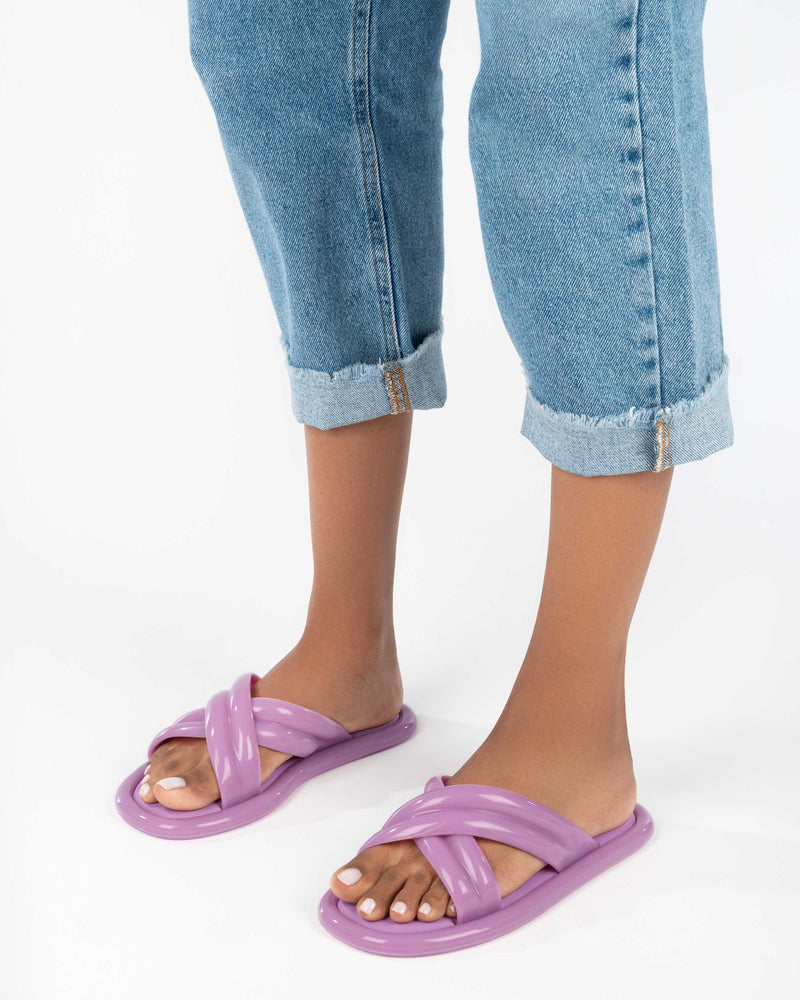 A model's legs wearing a pair of lilac Melissa Cali slides with cross straps.