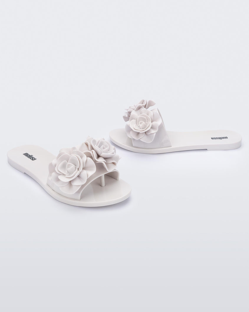 An angled front and side view of a pair of white Melissa Babe Garden slides with two flowers on the front strap.
