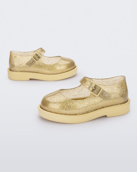 Side view of a pair of clear glitter yellow Mini Melissa Lola loafers with a rounded toe, strap and yellow buckle.