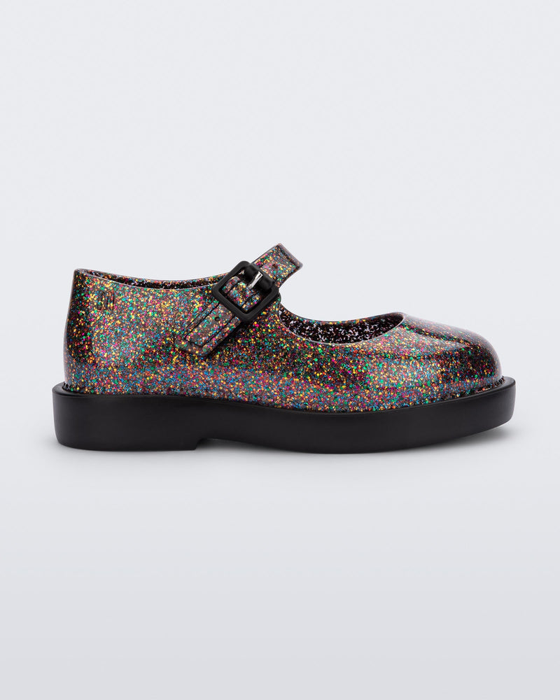 Side view of a clear multicolor glitter Mini Melissa Lola loafer with a rounded toe, strap and black buckle.