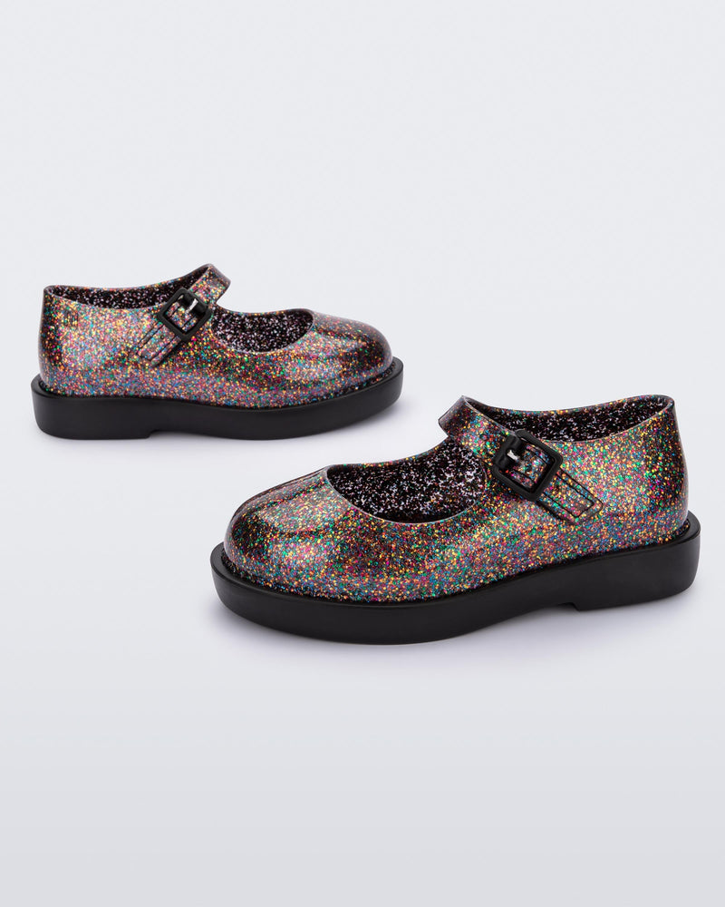 Side view of a pair of clear multicolor glitter Mini Melissa Lola loafer with a rounded toe, strap and black buckle.