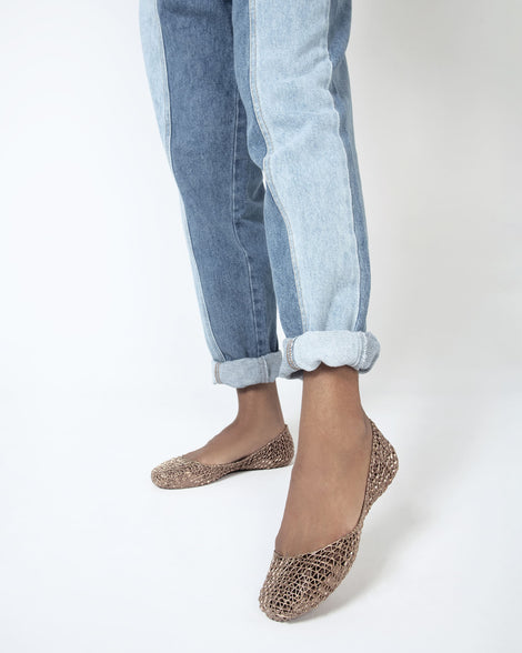 A close up of a model's legs with a pair of metallic gold Melissa Campana flats worn with cuffed jeans.