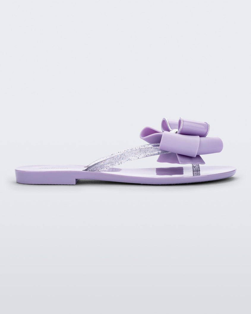 Side view of a lilac Melissa Harmonic Sweet flip flop with a lilac bow and clear glitter straps.