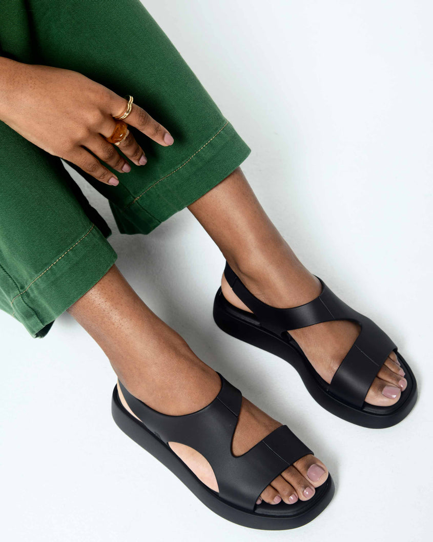 A model's legs wearing a pair of black Melissa Franny sandals with straps.
