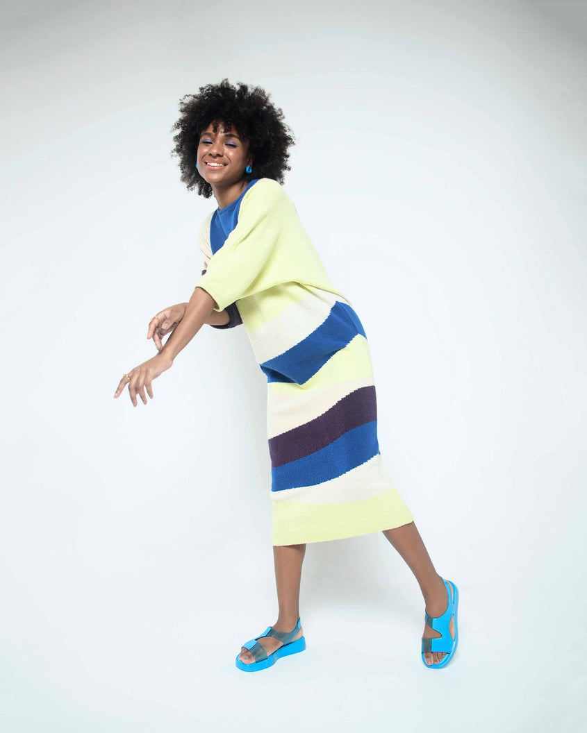 A model posing for a picture wearing a striped dress and a pair of blue Melissa Franny sandals with straps.