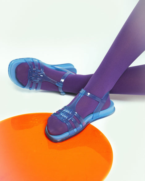 Model's legs waring purple tights and a pair of Melissa Party sandals in transparent blue with back ankle strap and buckle closure