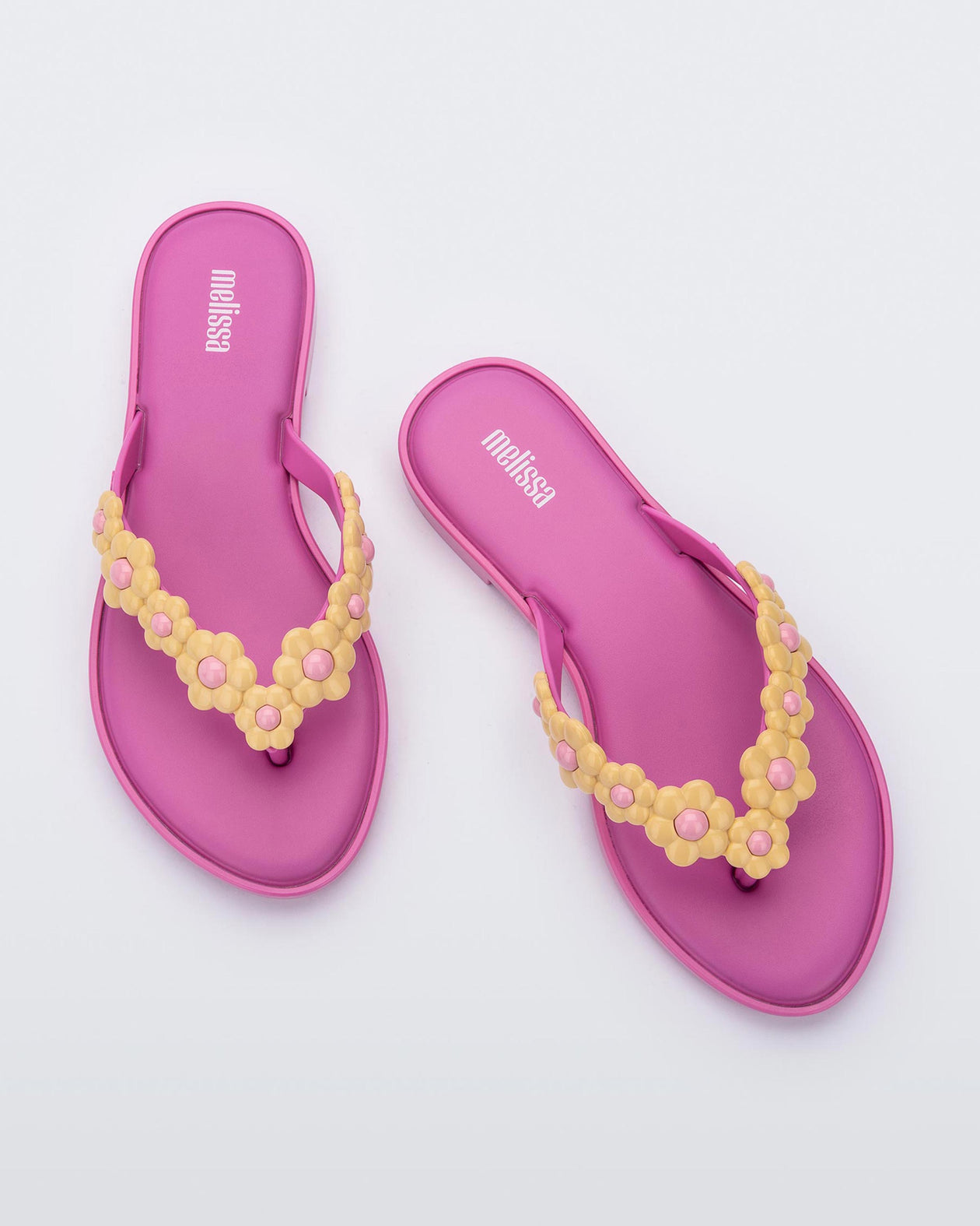 A top view of a pair of pink Melissa Spring Flip Flops with pink and yellow flowers on them.