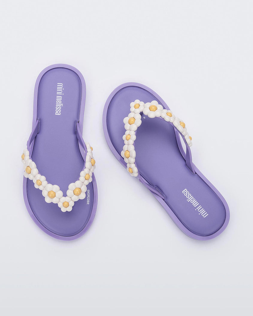 A top view of a pair of lilac Mini Melissa Spring Flip Flops with yellow and white flowers.