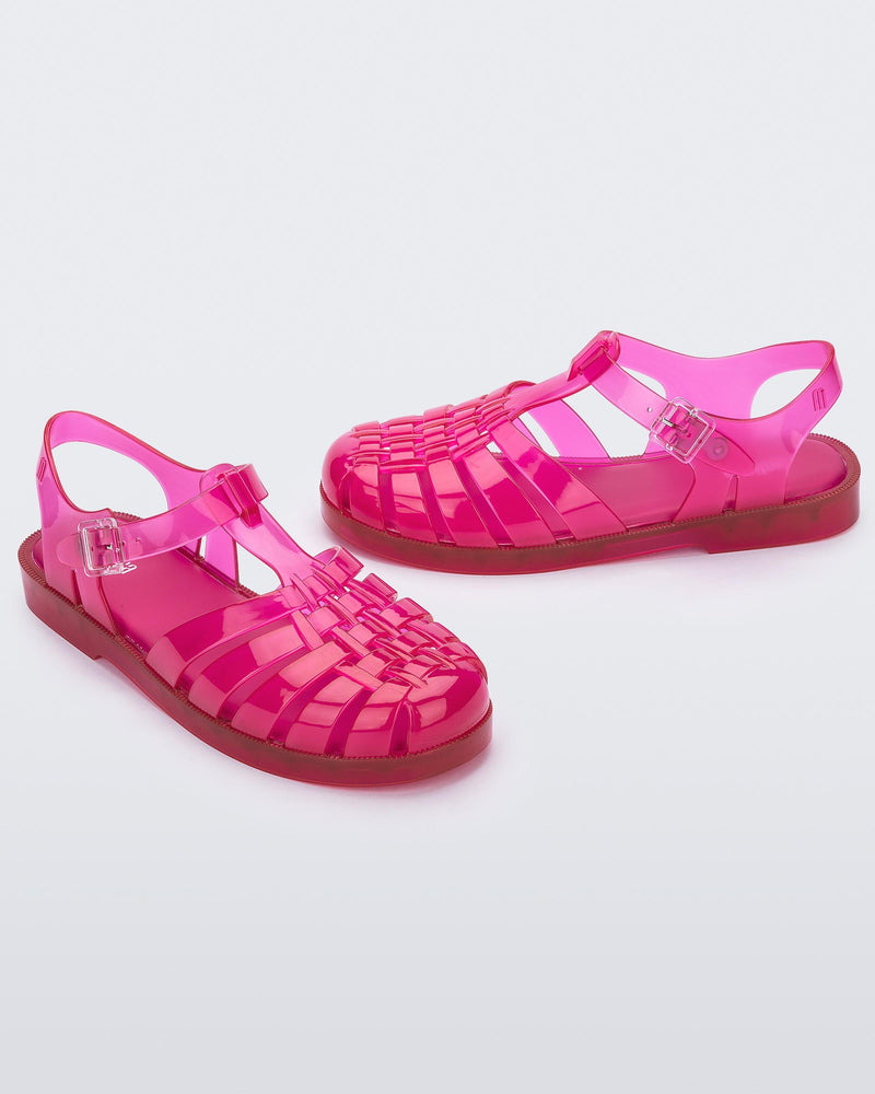 Angled view of a pair of transparent pink Melissa Possession sandal with a closed toe front weft design connected to a top strap with a buckle.