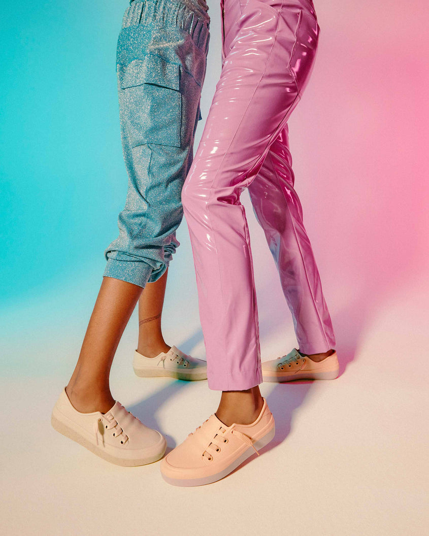 Two models' legs wearing a pair of pink and beige Melissa Ulitsa sneakers.