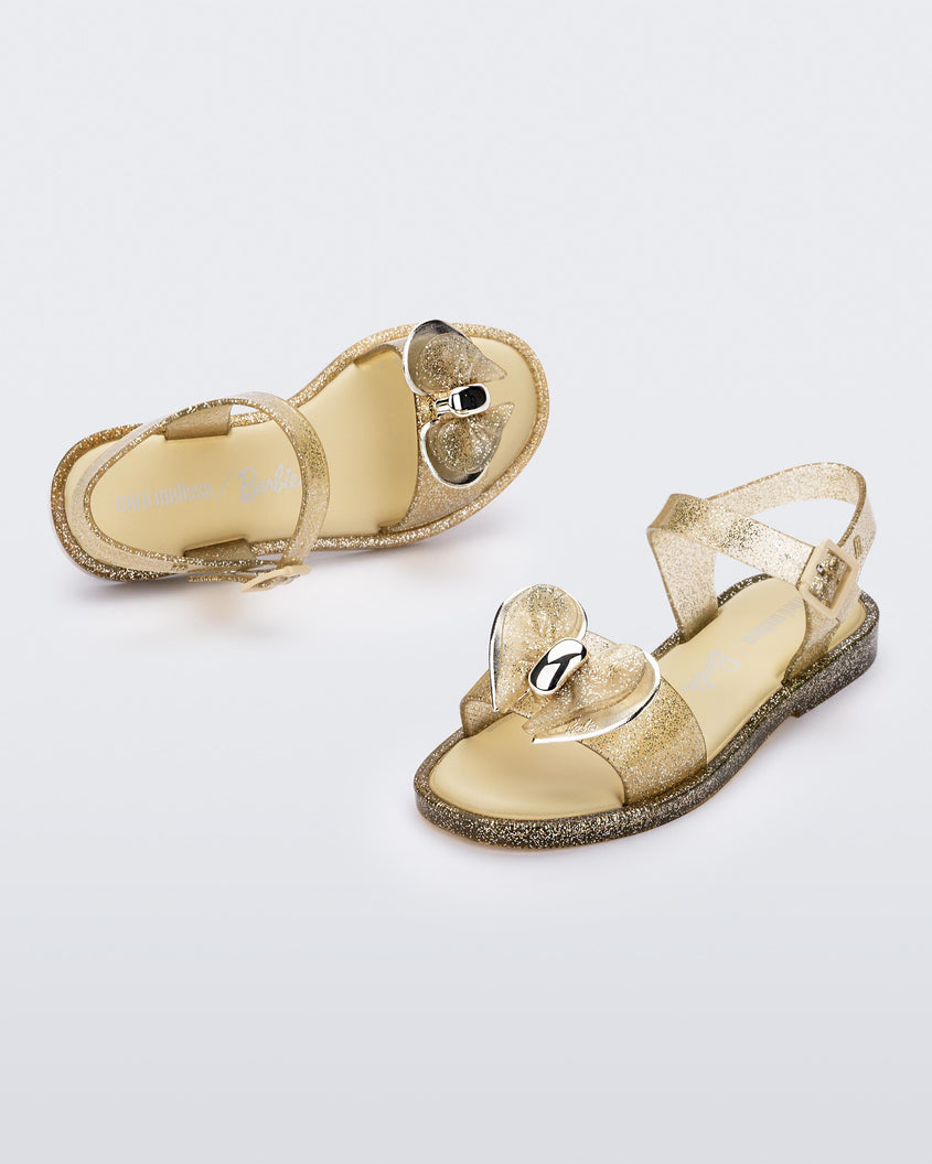 Angled view of a pair of gold glitter Mini Melissa Mar sandals with bows.