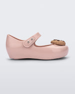 Side view of a Mini Melissa Ultragirl Candy ballet flat in Pink colorway. The shoe has a single strap across the top of the foot with a double snap closure. The product also has a 3D chocolate chip cookie applique on the top fo the toe. The cookie applicque is a light brown color with darker brown colored chips.
