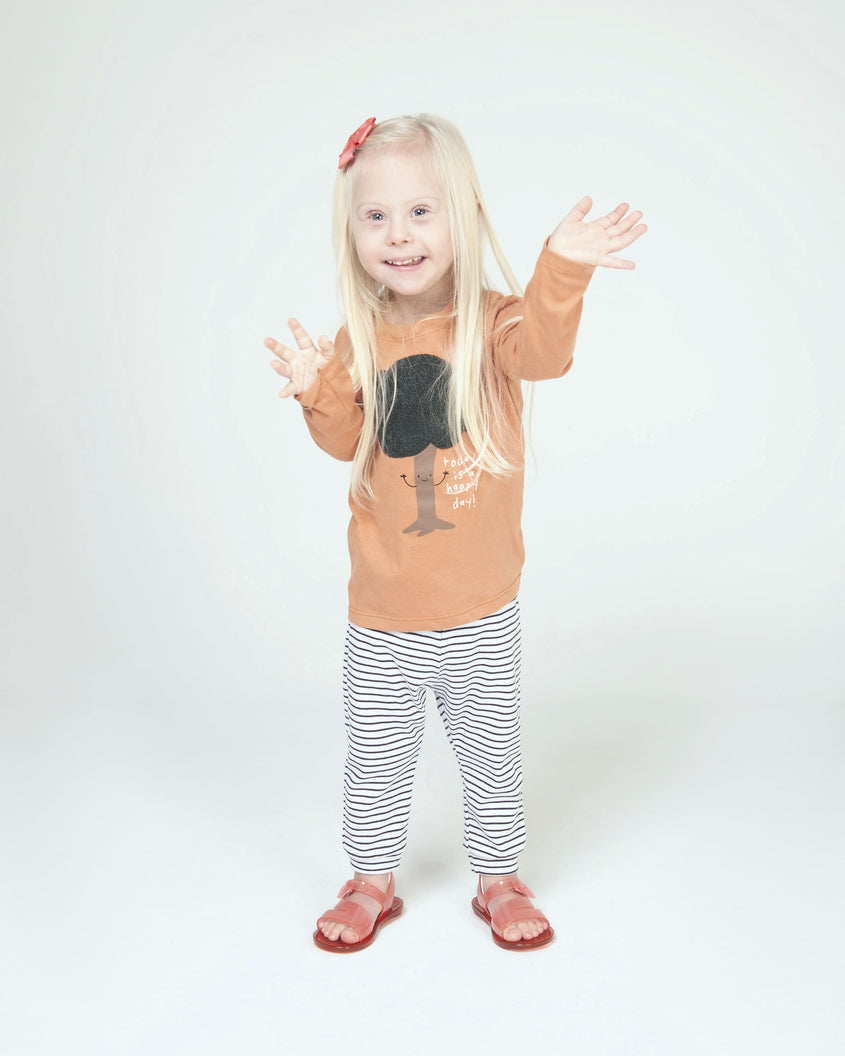 A young model in an orange top, black and white pants and a pair of pink/red Mini Melissa The Real Jelly Paris sandals with three front straps and a back ankle strap.