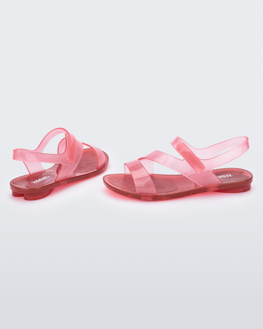 A side and back view of a pair of pink/red Mini MelissaThe Real Jelly Paris sandals with three front strap and an ankle straps with a clear pink/red glitter base.