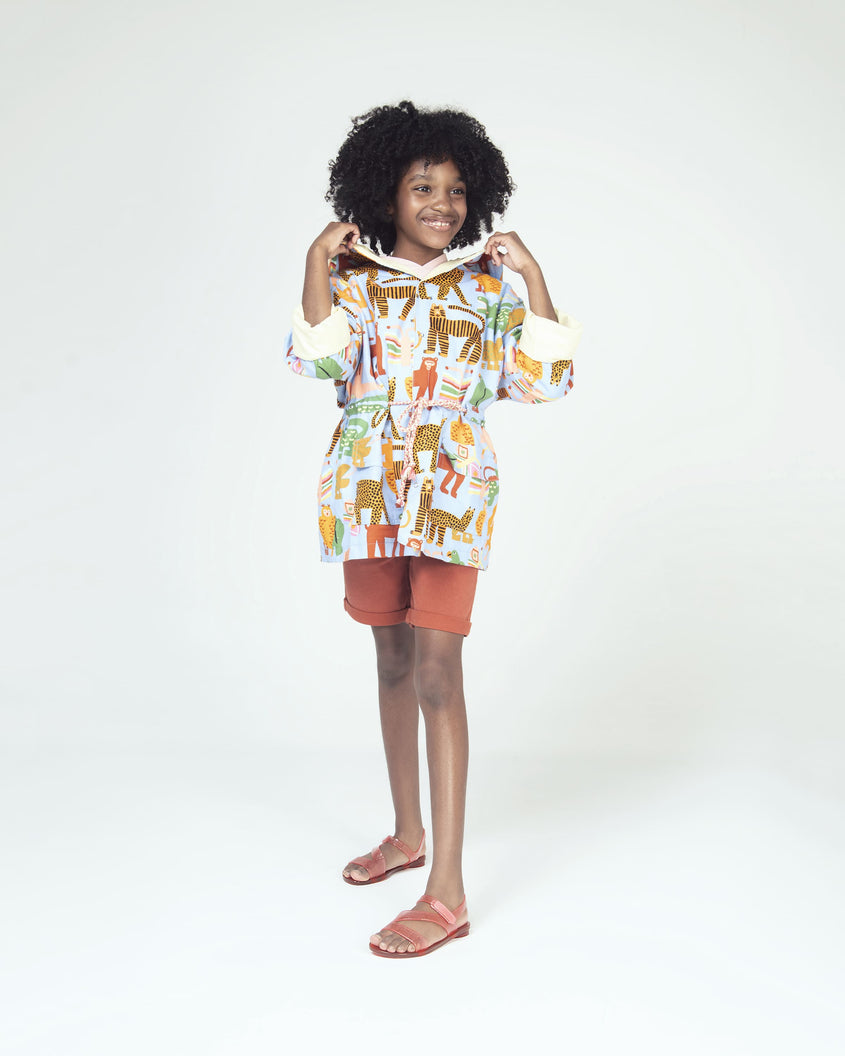 A model posing for a picture in a patterned top, brown shorts and a pair of pink/red Mini Melissa The Real Jelly Paris sandals with three front straps and an ankle strap with a clear pink/red glitter base.