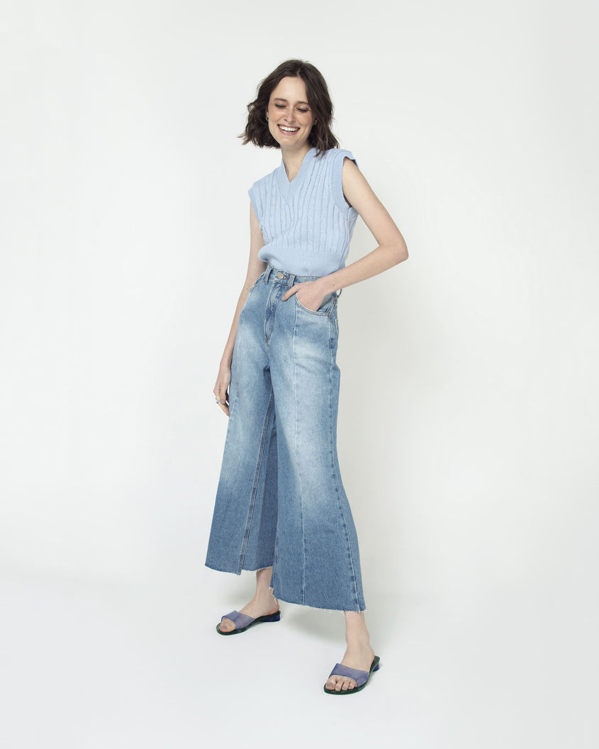 A model's posing for a picture in a top, jeans and a pair of transparent blue/green Melissa Kim slides.