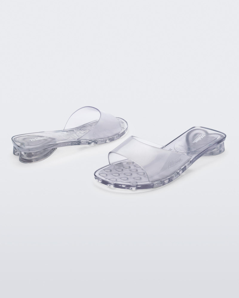 An angled front and side view of a pair of transparent clear Melissa Kim slides.