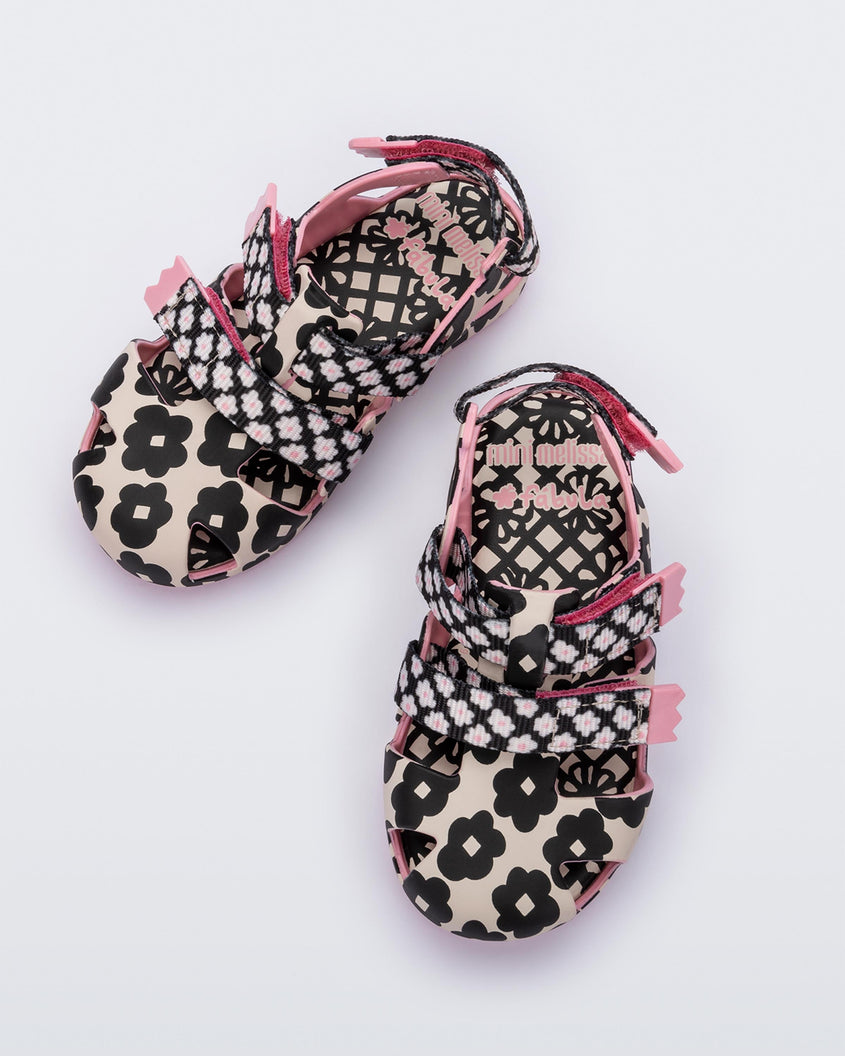 Top view of a pair of pink/black sandals Mini Melissa Yoyo with a pink and black floral base, two velcro front straps and a back ankle strap.
