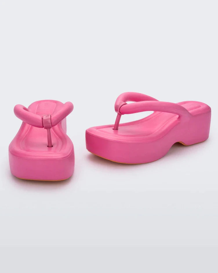 An angled front and side view of a pair of pink Melissa Free Platform Flip Flops with puffer-like straps.