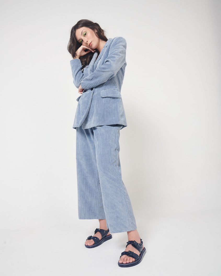 A model posing for a picture in a blue corduroy suit and a pair of blue Melissa Spikes Sandals with two straps with buckles on top and spike details around the base.