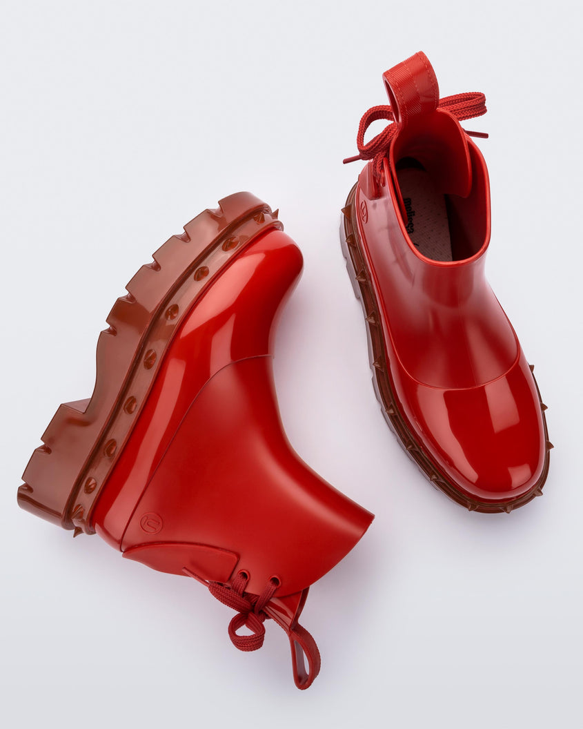 A side and top view of a pair of red Melissa Spikes Boots with spike details around the sole and laces in the back.