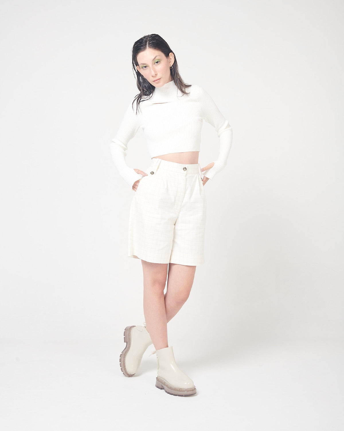 A model posing for a picture in a white top, white bottoms and a pair of beige Melissa Spikes Boots with spike details around the sole and laces in the back.