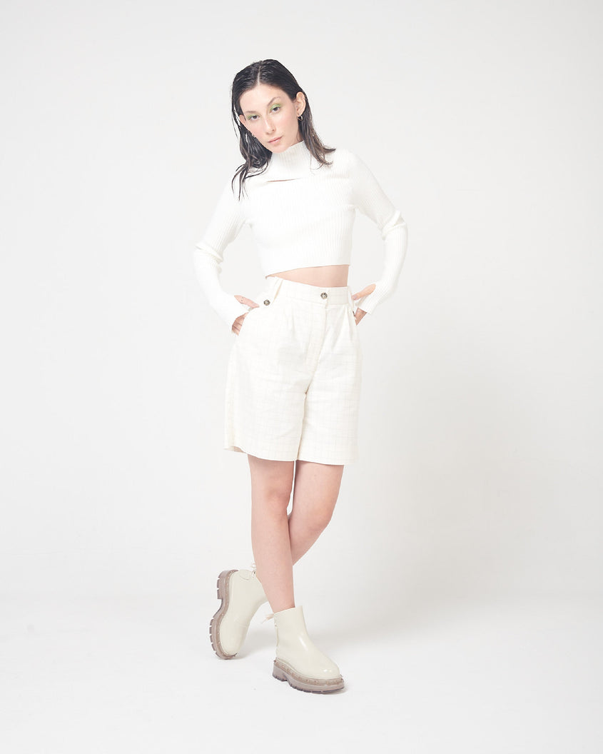 A model posing for a picture in a white top, white bottoms and a pair of beige Melissa Spikes Boots with spike details around the sole and laces in the back.