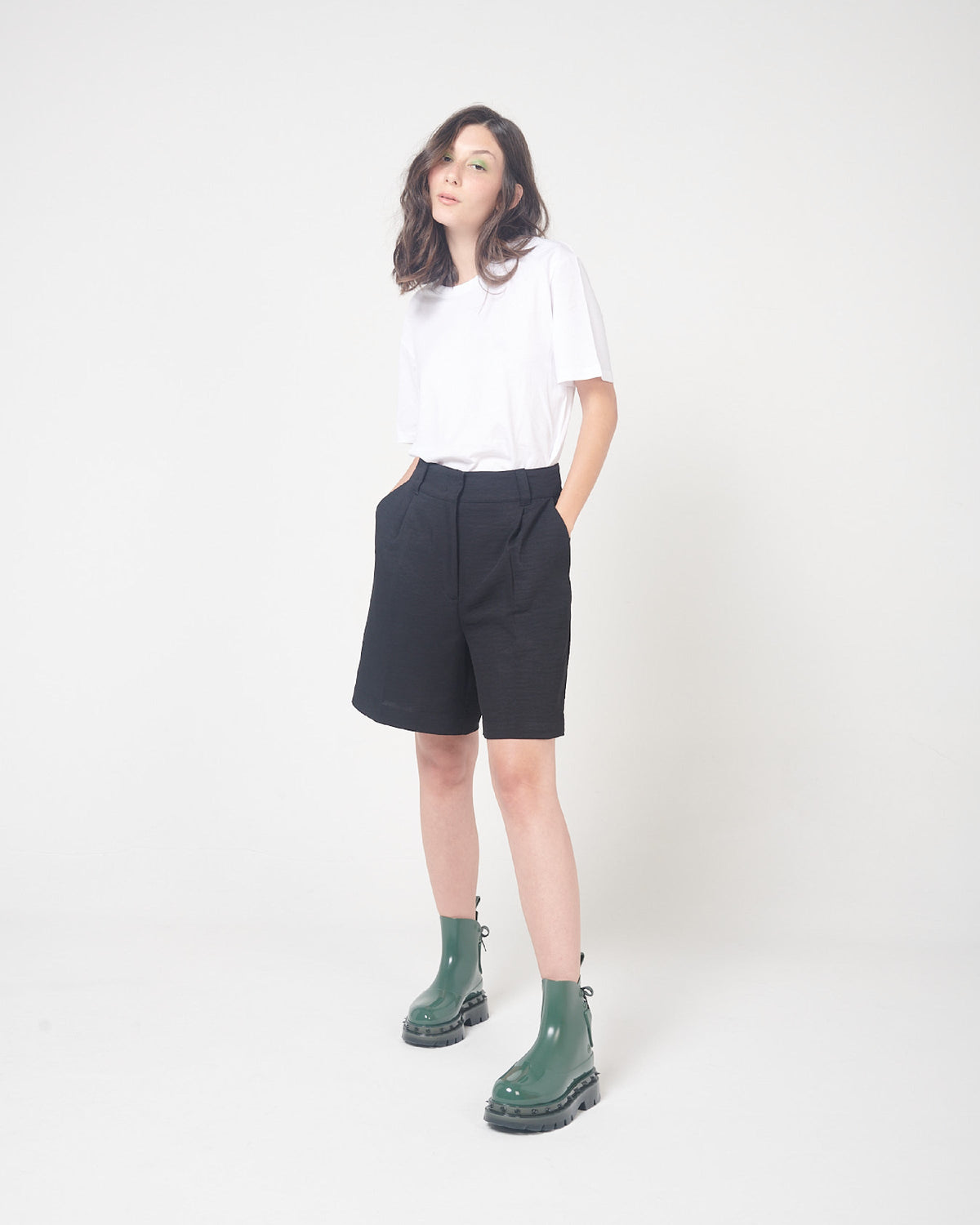 A model posing for a picture in a white top, black bottoms and a pair of green Melissa Spikes Boots with spike details around the sole and laces in the back.