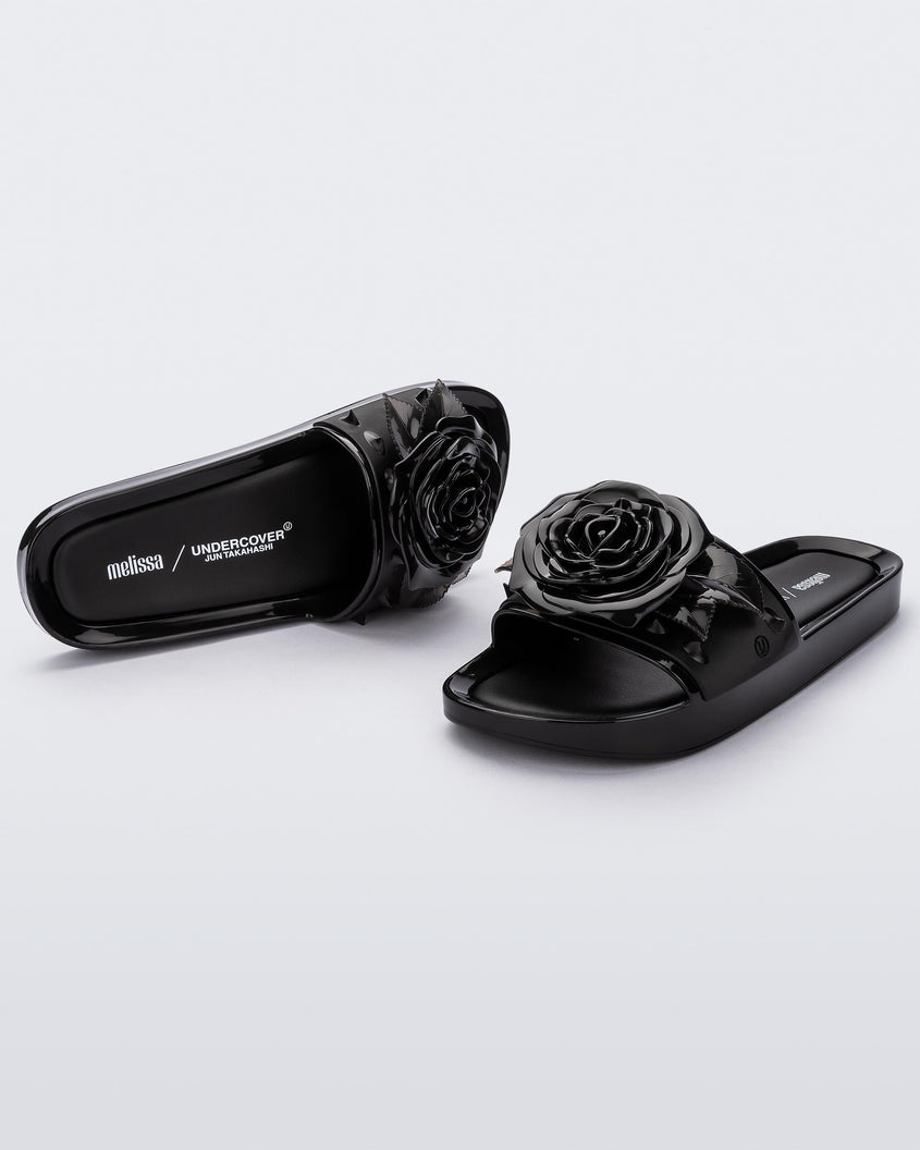 An angled front and side view of a pair of black Melissa Spikes Beach slides with a flower detail and spikes on the front strap.