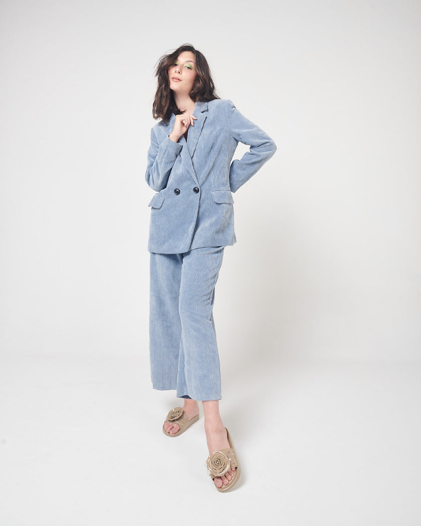 A model in a blue corduroy suit and a pair of beige Melissa Spikes Beach slides with a flower detail and spikes on the front strap.