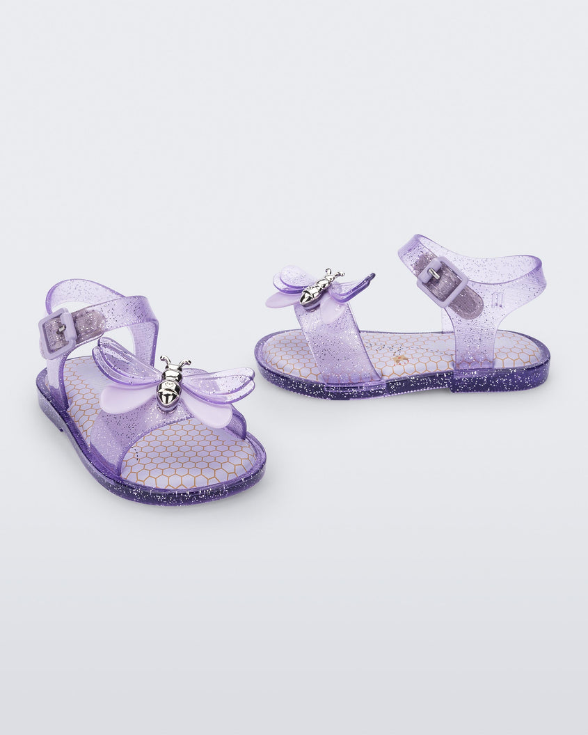 An angled front and side view of a pair of lilac glitter Mini Melissa Mar Bugs sandals with a honeycomb pattern insole and a lilac bug detail with a silver buckle on the front.