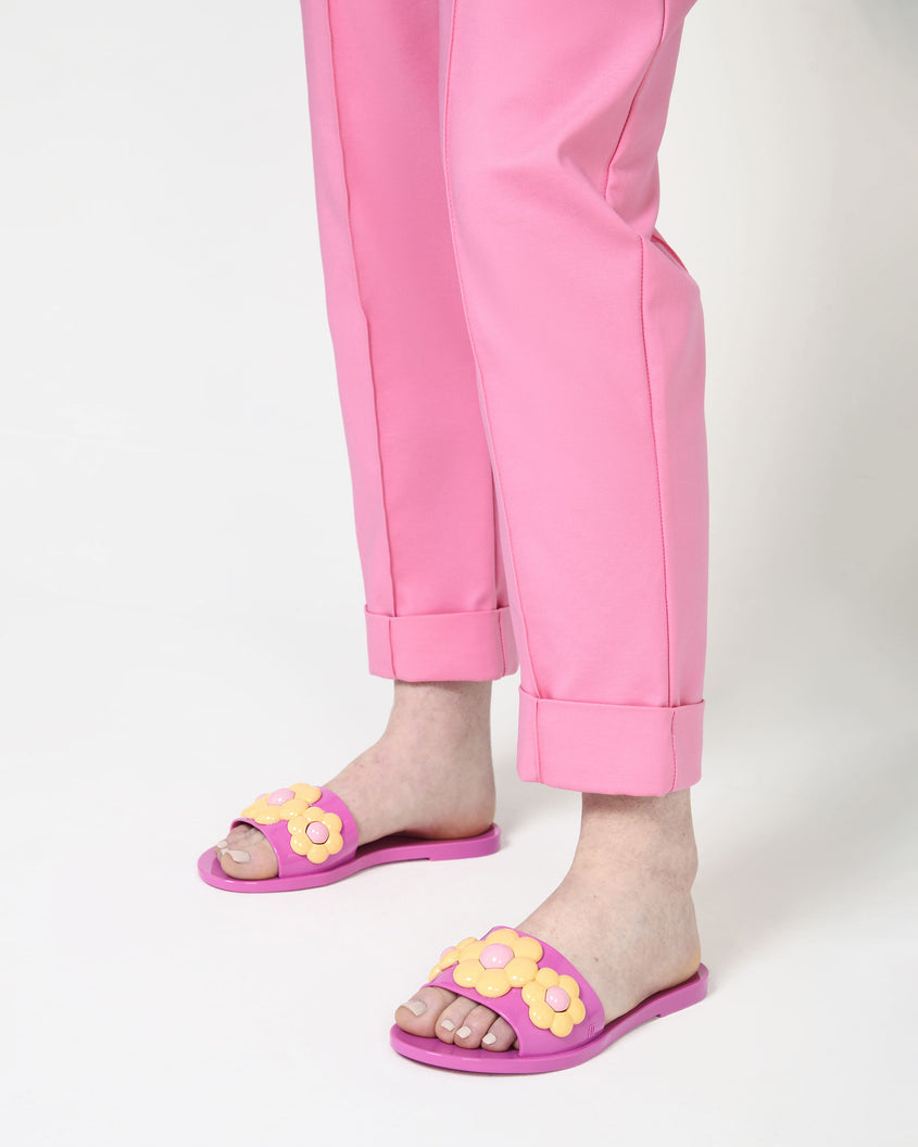 A mode's legs wearing a pare of pink Babe Spring Melissa slides with yellow flowers.