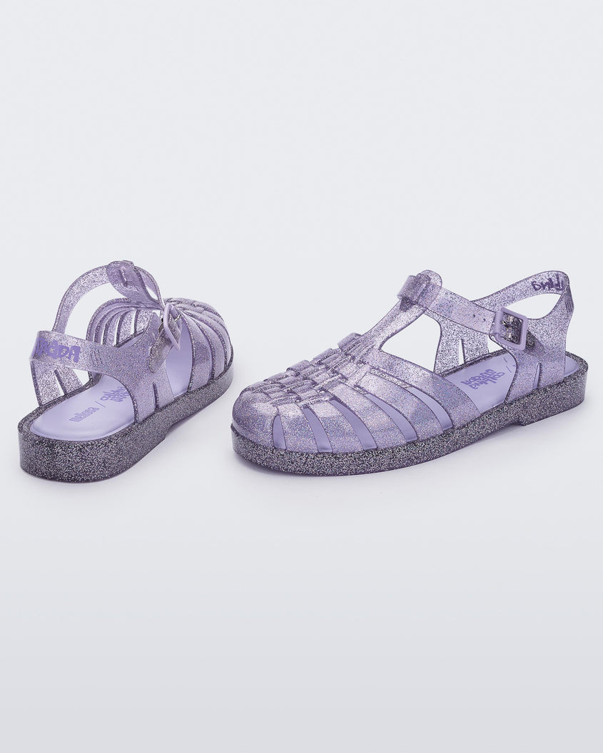 An angled side and back view of a pair of glitter lilac Melissa Possession sandals with several straps and a closed toe front.
